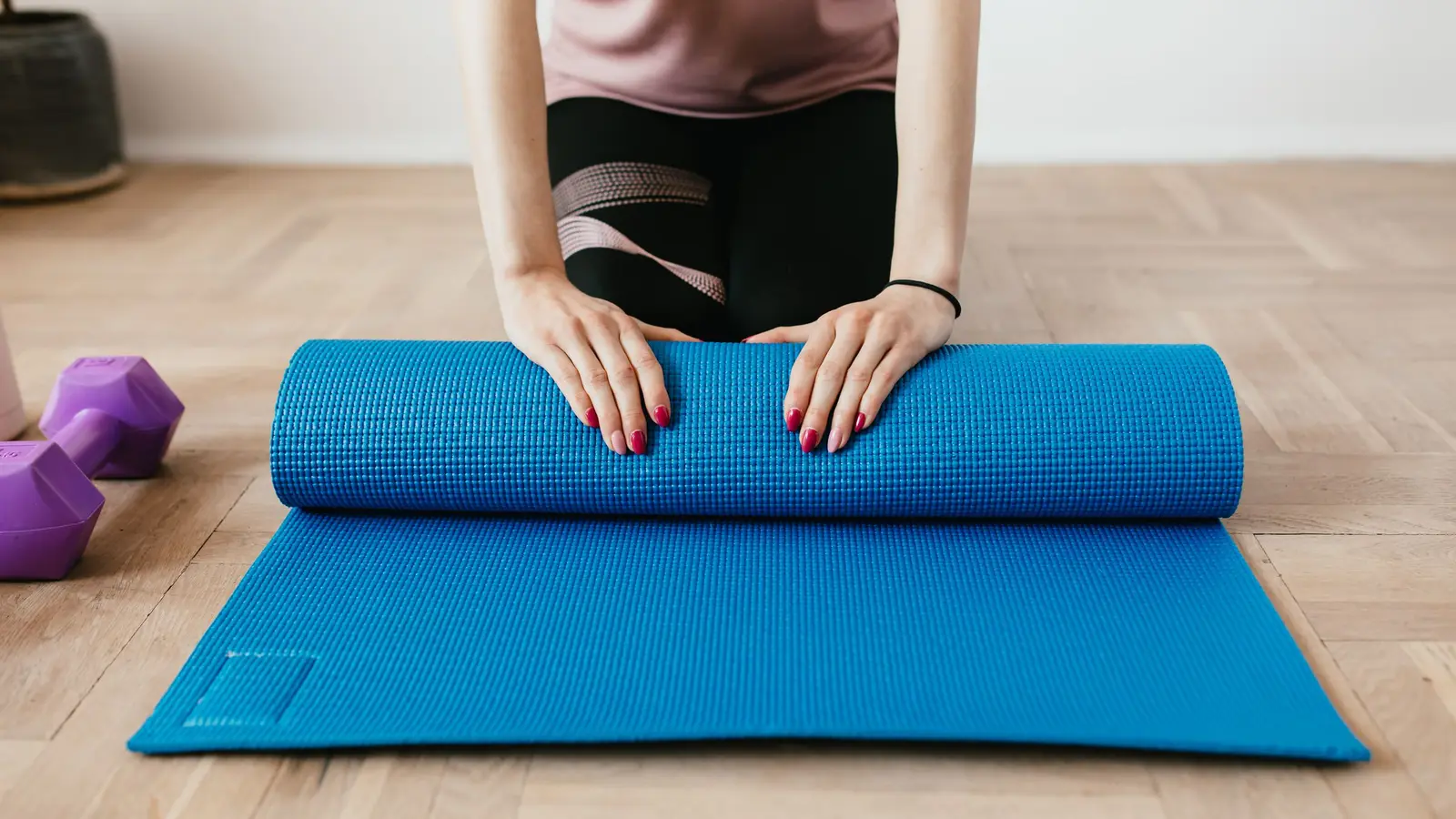 Personne déroulant un tapis bleu pour préparer une séance de sport à domicile.